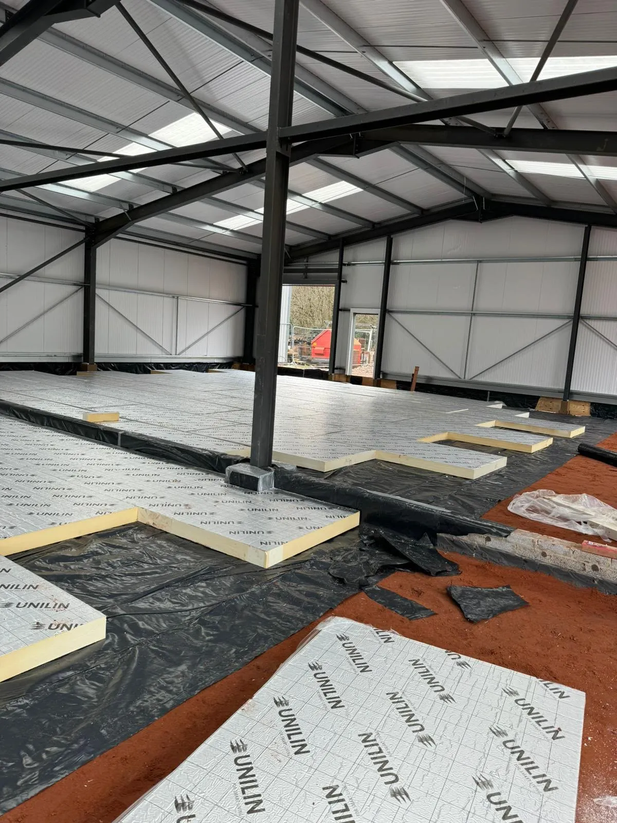 Floor insulation being laid inside a new steel frame building before the floor is finished