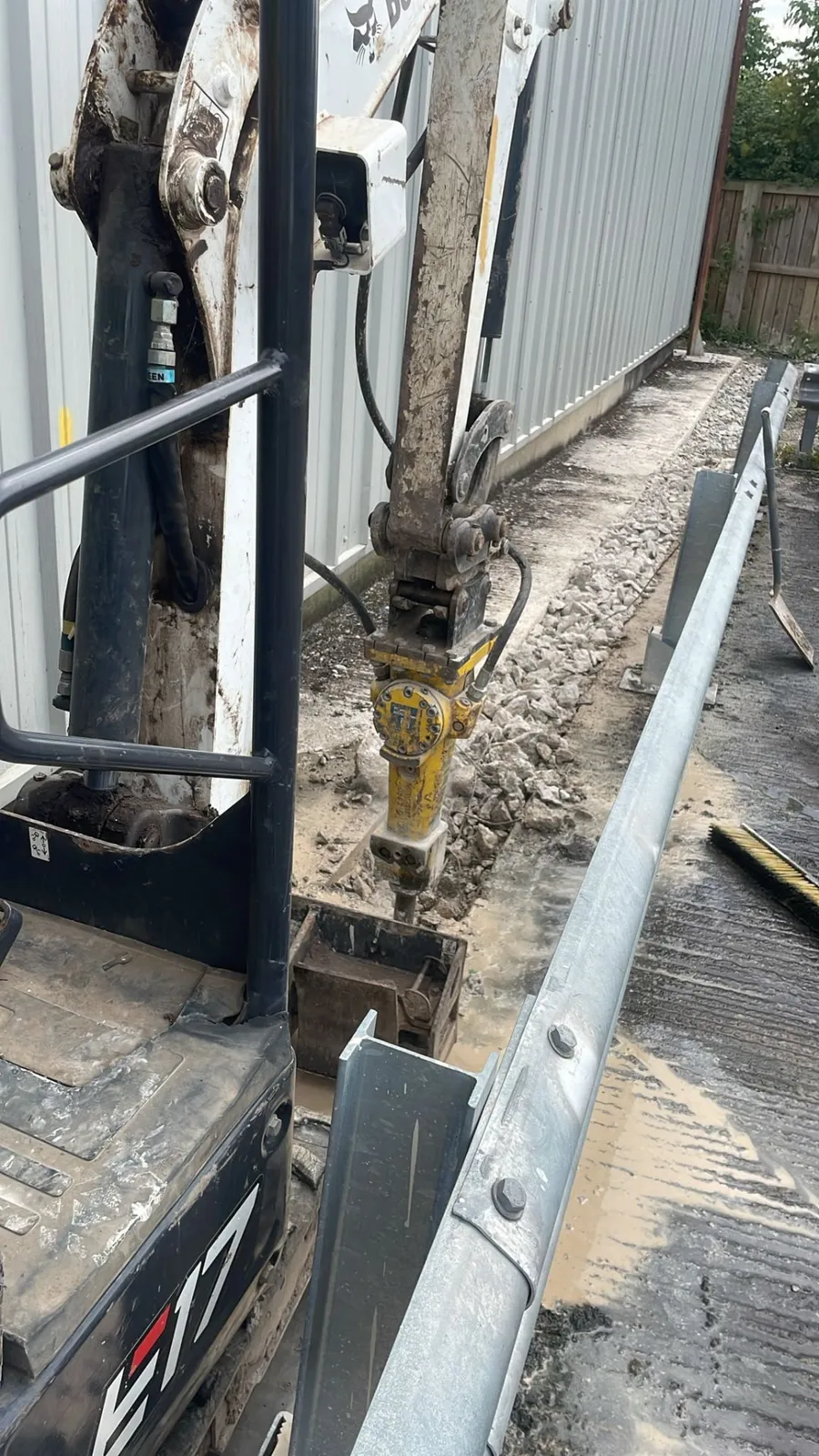 Excavator breaker removing concrete hardstanding beside a commercial building