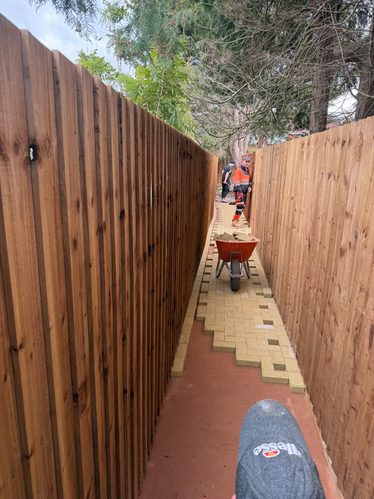 Groundworkers laying a block paved pathway between fences on a domestic property