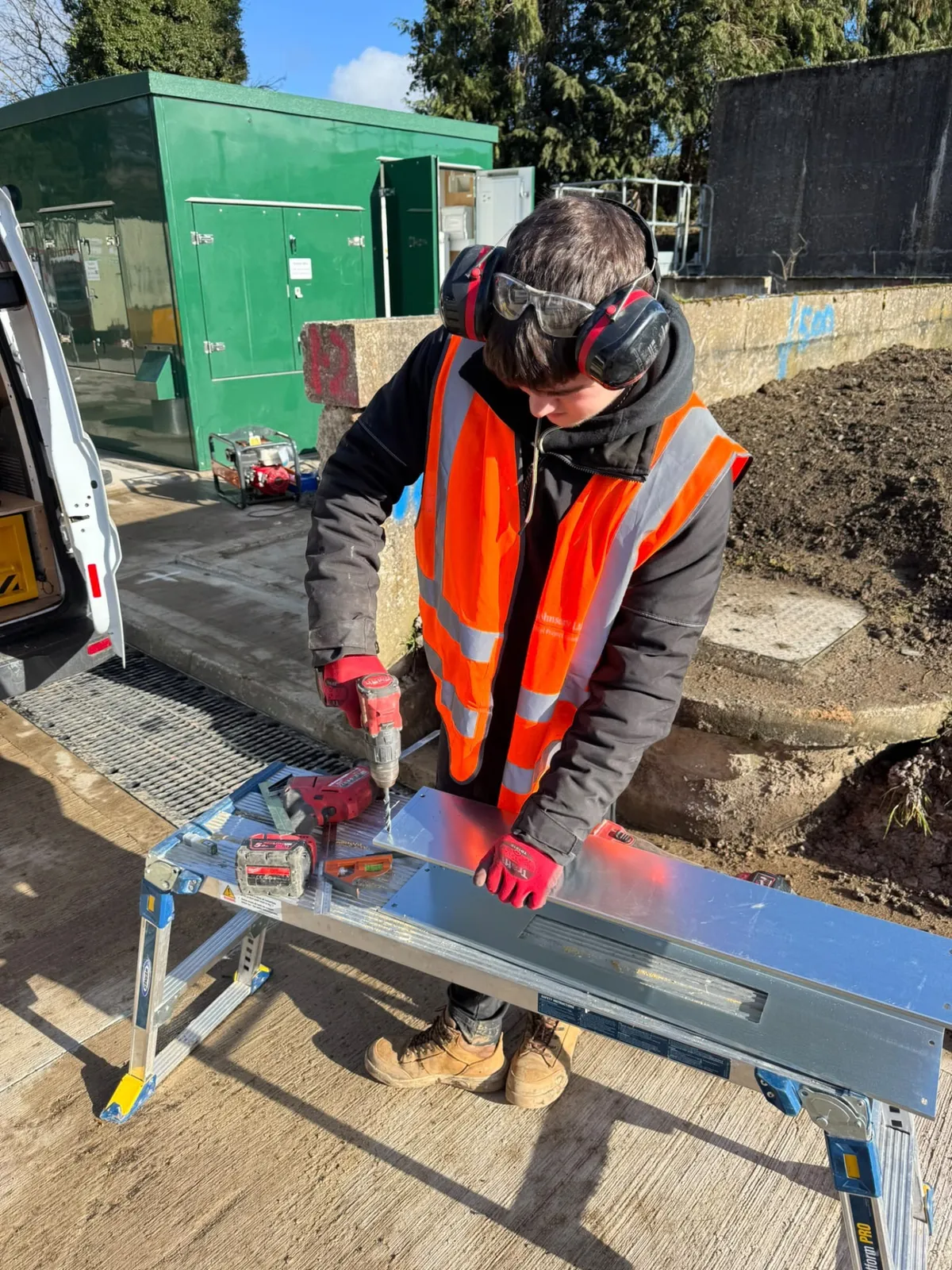 Electrician in PPE cutting cable tray on a trestle during a commercial installation in the West Midlands